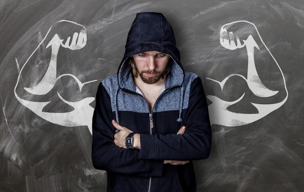 mental strength, man in hoodie with arms crodded, eyes down, against chalkboard drawing of muscled arms